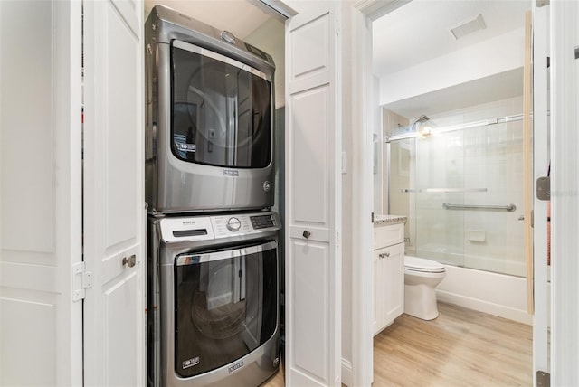 laundry area featuring stacked washing maching and dryer and light hardwood / wood-style flooring