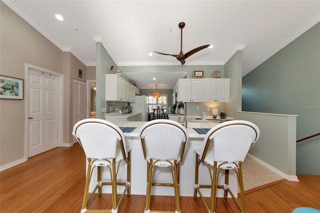 kitchen with white fridge, light wood-type flooring, kitchen peninsula, ceiling fan, and white cabinets