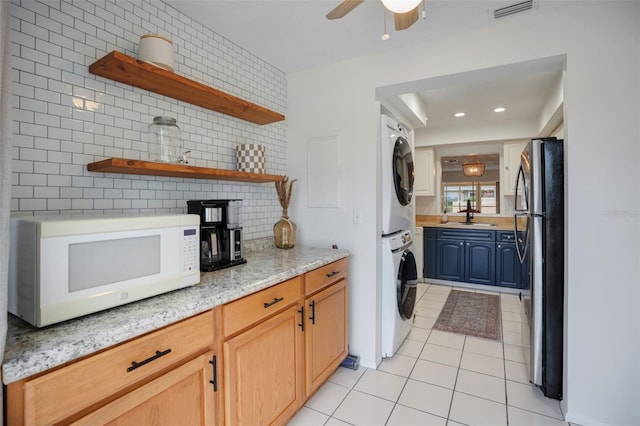 kitchen with sink, stacked washing maching and dryer, light tile patterned floors, decorative backsplash, and stainless steel refrigerator