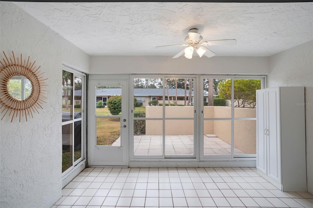 doorway to outside with ceiling fan, light tile patterned flooring, and a textured ceiling