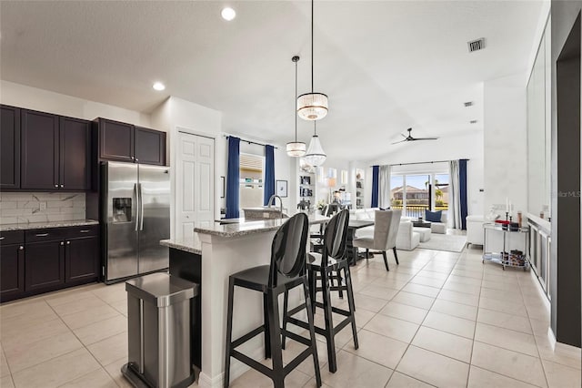 kitchen with decorative light fixtures, stainless steel fridge, light tile patterned flooring, and a center island with sink