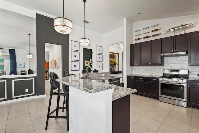 kitchen with decorative light fixtures, stainless steel range with gas cooktop, a kitchen breakfast bar, light stone countertops, and a kitchen island with sink