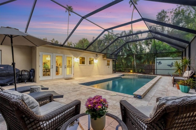 pool at dusk with area for grilling, a patio area, glass enclosure, and a storage shed