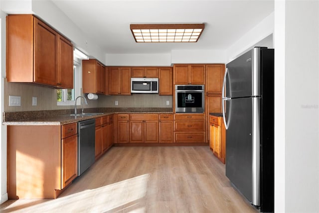 kitchen with dark stone countertops, stainless steel appliances, light wood-type flooring, sink, and tasteful backsplash