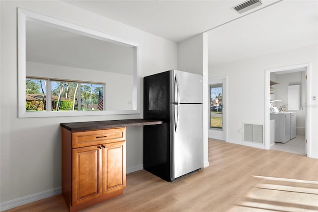 kitchen featuring washer and dryer, stainless steel refrigerator, and light wood-type flooring