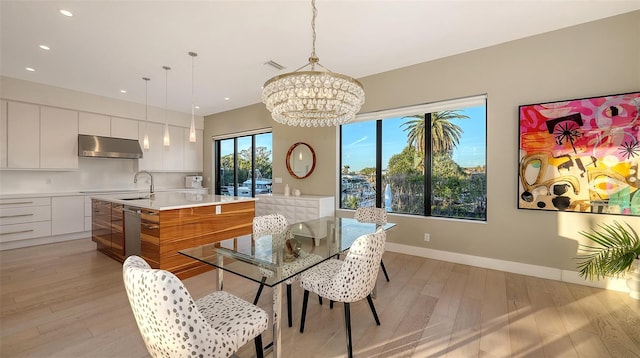 dining room featuring sink, a notable chandelier, light hardwood / wood-style flooring, and a healthy amount of sunlight