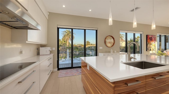 kitchen with extractor fan, an island with sink, sink, white cabinets, and hanging light fixtures