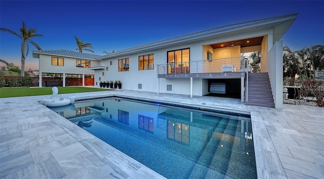 back house at dusk featuring a balcony, a pool with hot tub, and a patio