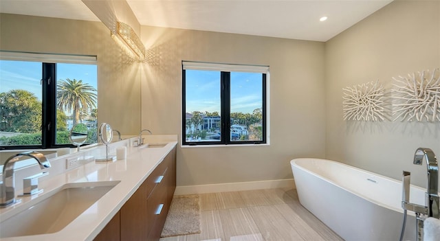 bathroom with a freestanding bath, double vanity, a sink, and baseboards