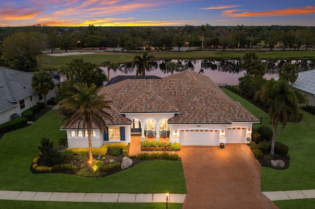 view of front facade featuring a water view, a garage, and a lawn