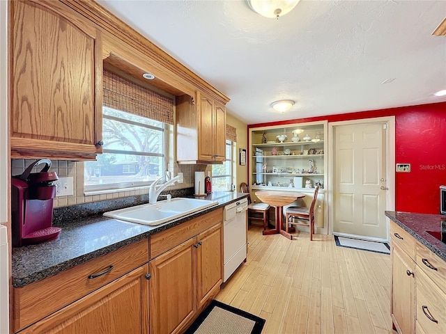 kitchen with backsplash, dishwasher, dark stone countertops, sink, and light hardwood / wood-style flooring