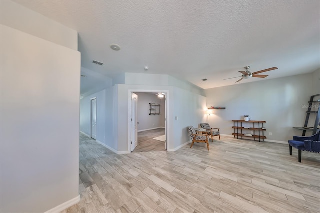 living area featuring ceiling fan, light wood-type flooring, and a textured ceiling