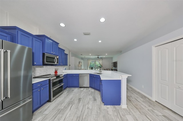 kitchen with blue cabinets, kitchen peninsula, appliances with stainless steel finishes, and tasteful backsplash