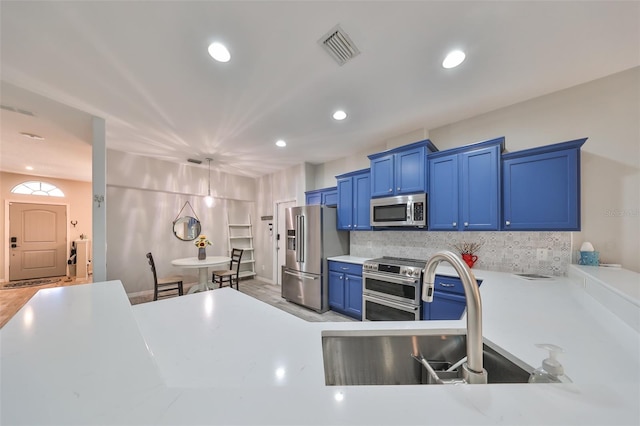 kitchen featuring sink, blue cabinetry, backsplash, pendant lighting, and appliances with stainless steel finishes