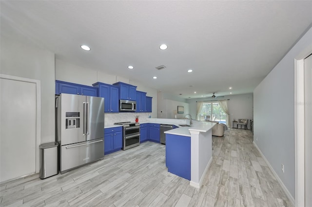 kitchen with stainless steel appliances, kitchen peninsula, ceiling fan, sink, and blue cabinets