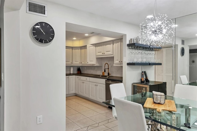 kitchen featuring backsplash, stainless steel dishwasher, sink, light tile patterned flooring, and a chandelier