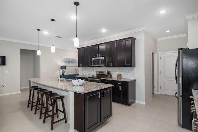 kitchen featuring light stone countertops, decorative light fixtures, stainless steel appliances, an island with sink, and sink