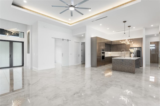 kitchen with appliances with stainless steel finishes, a barn door, french doors, pendant lighting, and an island with sink