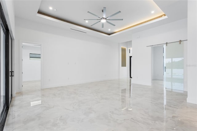 spare room with ceiling fan, a raised ceiling, and a barn door