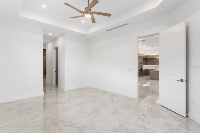 empty room featuring ceiling fan and a raised ceiling