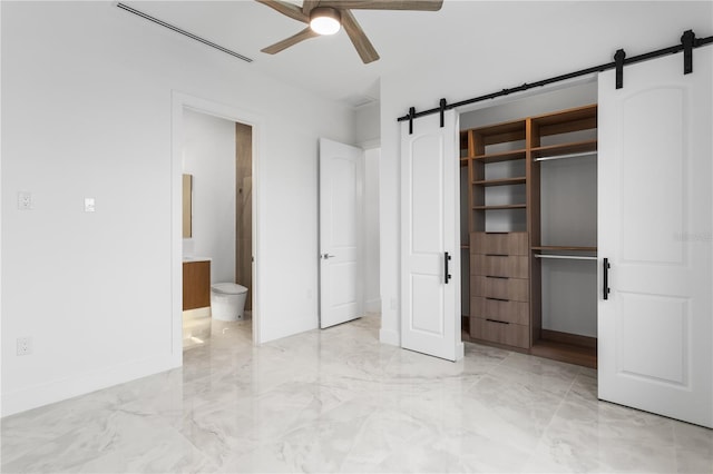 unfurnished bedroom featuring a closet, ceiling fan, a barn door, and ensuite bath