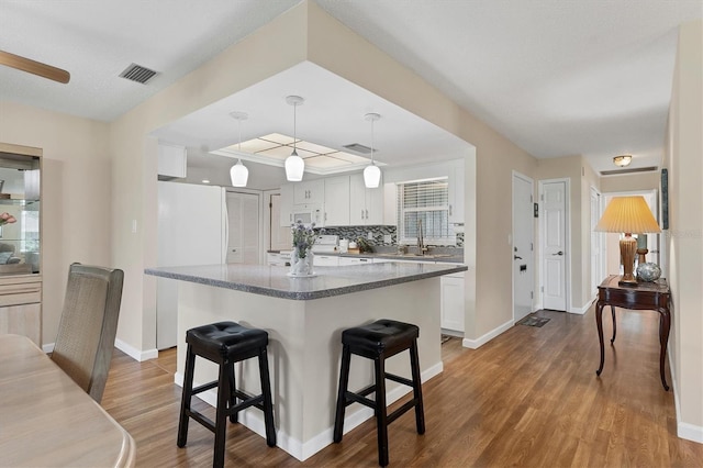 kitchen with a breakfast bar area, white appliances, wood finished floors, a sink, and visible vents