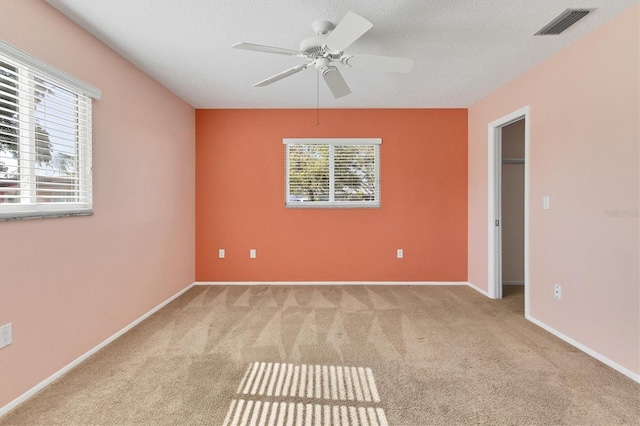 unfurnished room with light colored carpet, a healthy amount of sunlight, visible vents, and a textured ceiling