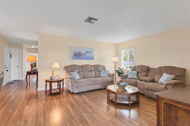 living room featuring visible vents, a textured ceiling, baseboards, and wood finished floors