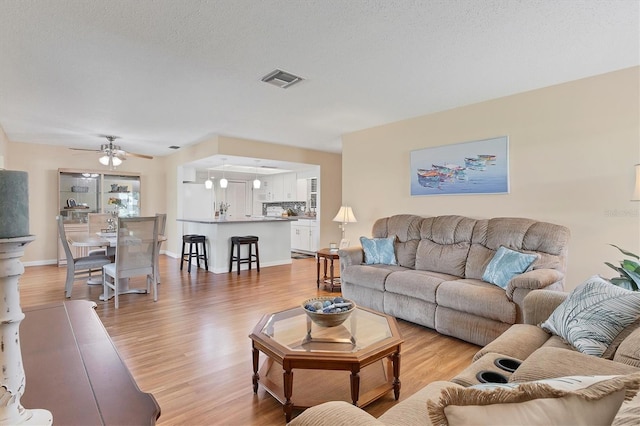 living area with a ceiling fan, visible vents, light wood-style flooring, and a textured ceiling