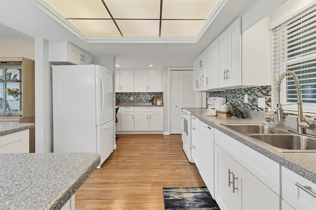 kitchen featuring white appliances, light wood-style flooring, a sink, white cabinetry, and backsplash