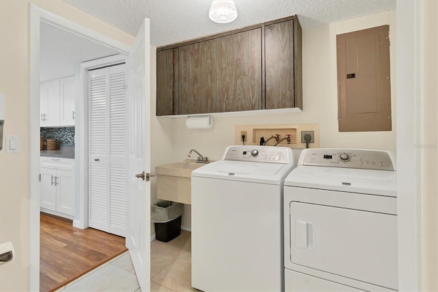 clothes washing area with light tile patterned floors, a textured ceiling, independent washer and dryer, cabinet space, and electric panel