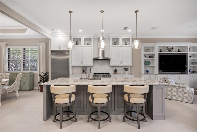 kitchen featuring white cabinetry, stainless steel built in refrigerator, an island with sink, sink, and hanging light fixtures