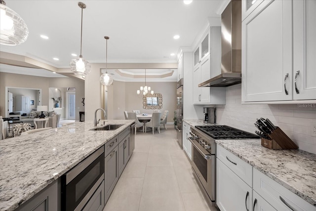 kitchen featuring appliances with stainless steel finishes, white cabinetry, wall chimney range hood, sink, and a tray ceiling