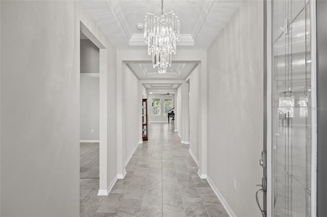 hall featuring a raised ceiling, ornamental molding, and a chandelier