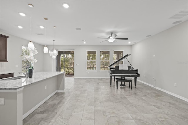 kitchen with light stone counters, pendant lighting, sink, ceiling fan with notable chandelier, and dark brown cabinetry