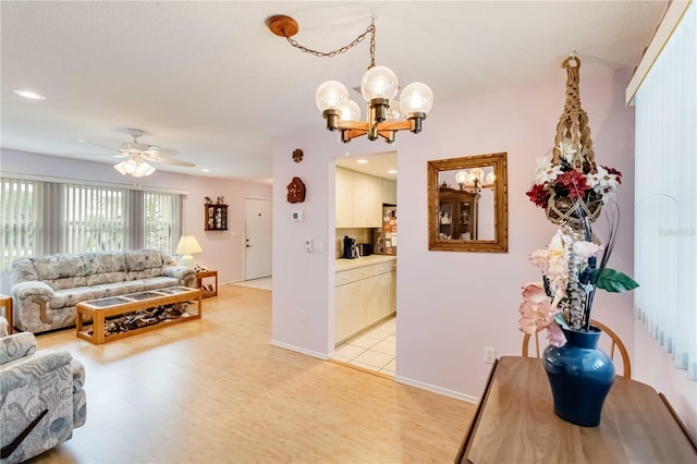 living room featuring ceiling fan with notable chandelier and light hardwood / wood-style flooring