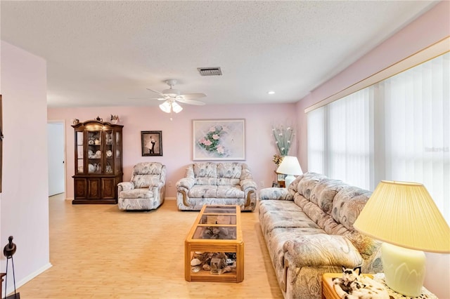 living room featuring ceiling fan, a textured ceiling, and light hardwood / wood-style flooring