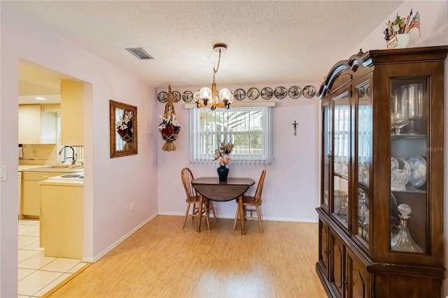 dining area with a notable chandelier, sink, a textured ceiling, and light hardwood / wood-style flooring