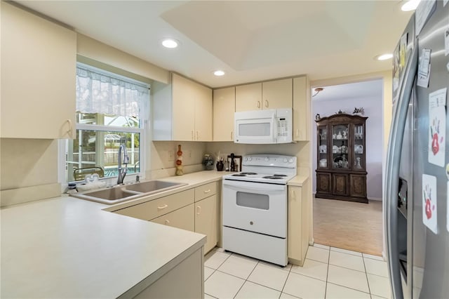 kitchen with light tile patterned floors, cream cabinetry, a tray ceiling, white appliances, and sink