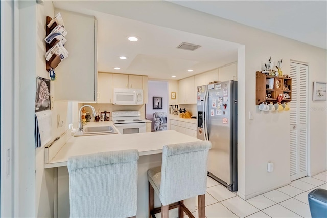 kitchen featuring white appliances, sink, kitchen peninsula, a breakfast bar, and light tile patterned floors