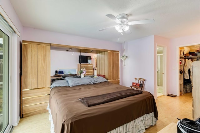 bedroom with light wood-type flooring, ceiling fan, a walk in closet, and a closet