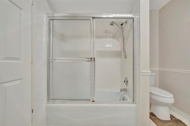 bathroom with toilet and shower / bath combination with glass door