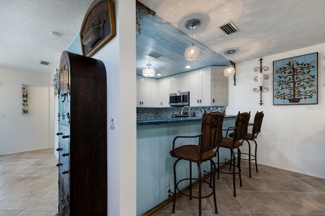 kitchen featuring decorative light fixtures, white cabinets, a kitchen breakfast bar, tasteful backsplash, and kitchen peninsula