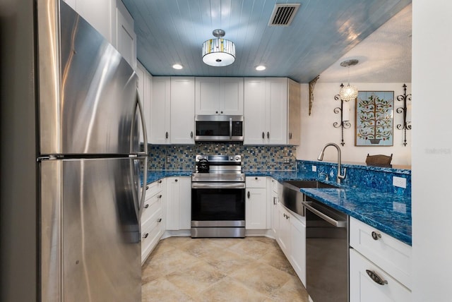 kitchen with pendant lighting, stainless steel appliances, white cabinets, dark stone counters, and sink