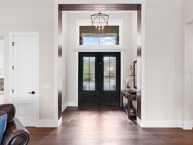 foyer entrance with dark wood-type flooring, a notable chandelier, and french doors