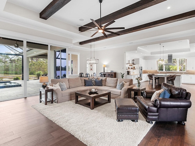 living room with hardwood / wood-style flooring, ceiling fan with notable chandelier, and a raised ceiling