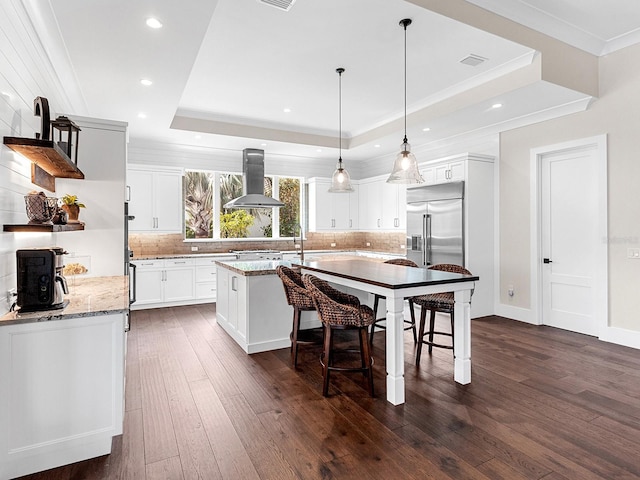 kitchen featuring extractor fan, a raised ceiling, hanging light fixtures, white cabinets, and light stone counters