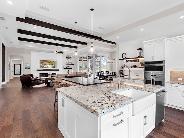 kitchen featuring pendant lighting, white cabinets, beamed ceiling, an island with sink, and light stone counters