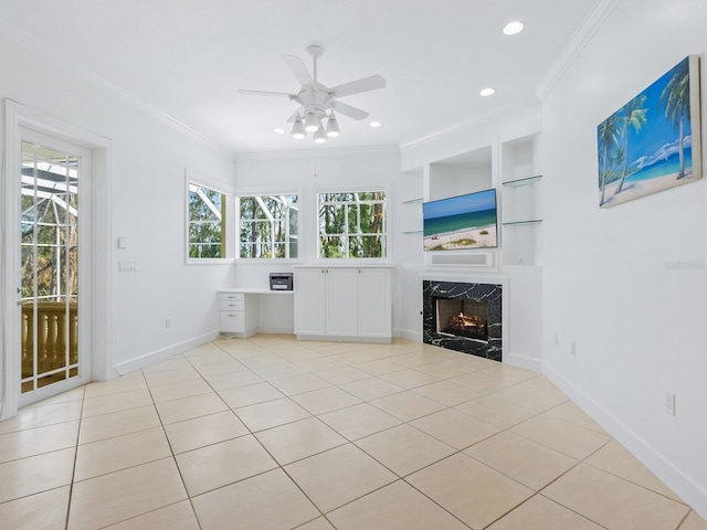 unfurnished living room featuring built in shelves, ornamental molding, a premium fireplace, ceiling fan, and light tile patterned flooring