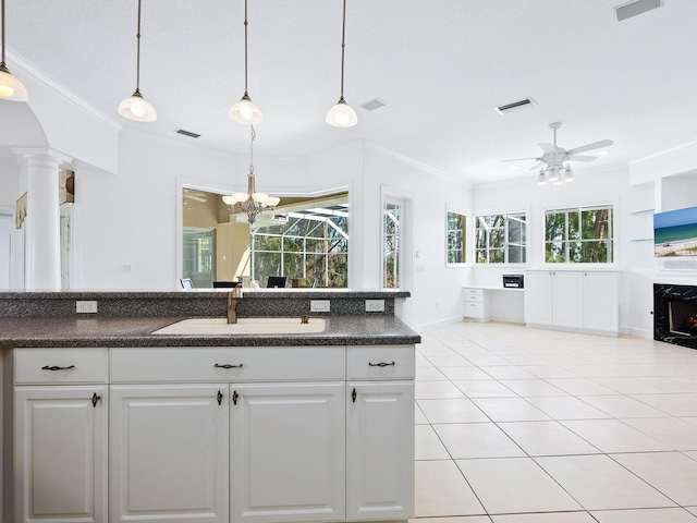 kitchen with a high end fireplace, crown molding, hanging light fixtures, white cabinets, and sink